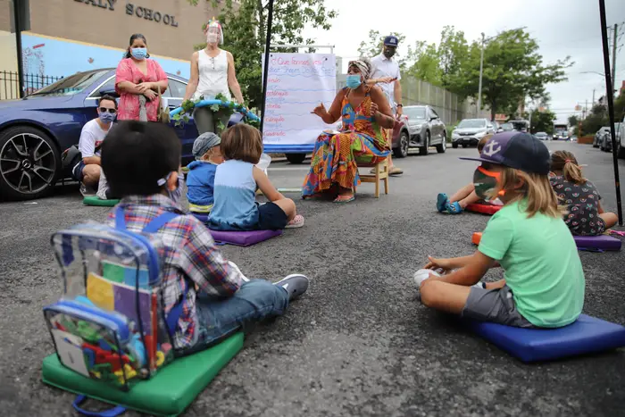 Children sit on mats outside in Red Hook